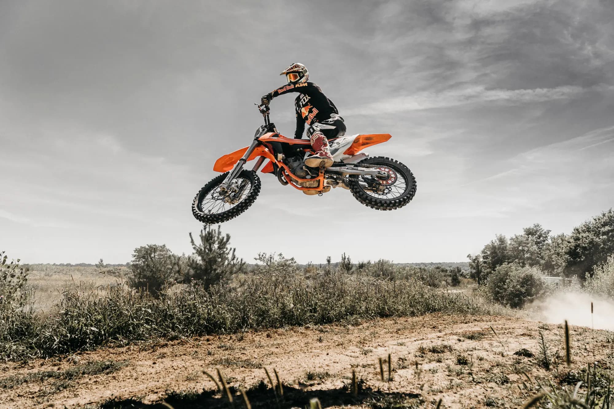 Motocross rider in full protective gear jumping a dirt bike over an outback track