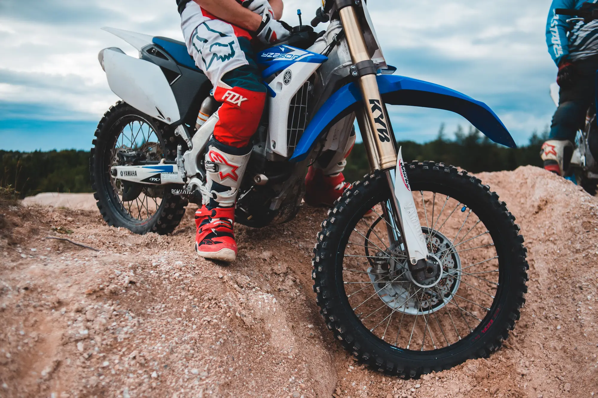 Close-up of a rider on a dirt bike at the crest of a dirt berm, wearing MX boots and gear