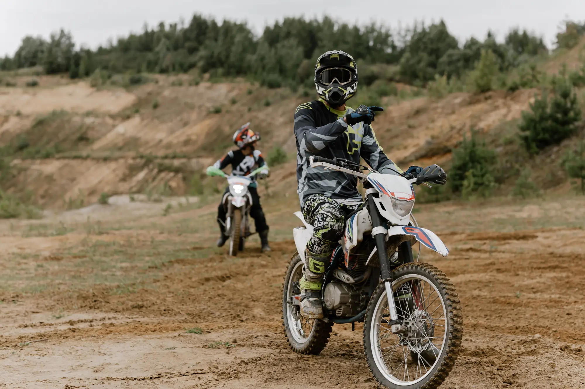 Two riders on dirt bikes on an Australian bush trail, one gesturing ahead